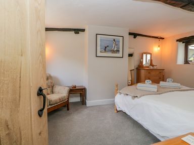 A bedroom with a bed with towels on it a wooden dresser a floral armchair and a painting on the wall at Ashness in Bassenthwaite near Keswick