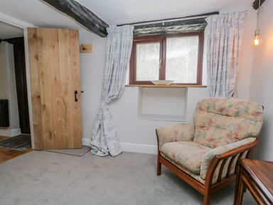 A room with a wooden door a window with curtains an armchair and a side table at Ashness in Bassenthwaite near Keswick