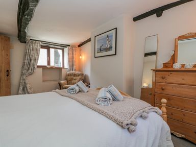 A bedroom with a bed covered with white linens and towels a wooden dresser a tall mirror an armchair and curtained window at Ashness in Bassenthwaite near Keswick