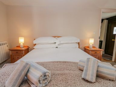 A bedroom with a bed with white linens and pillows two bedside tables with lamps and rolled towels on the bed at Ashness in Bassenthwaite near Keswick