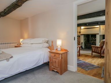 A bedroom with a bed and bedside table with lamp looking into a living room with a fireplace at Ashness in Bassenthwaite near Keswick