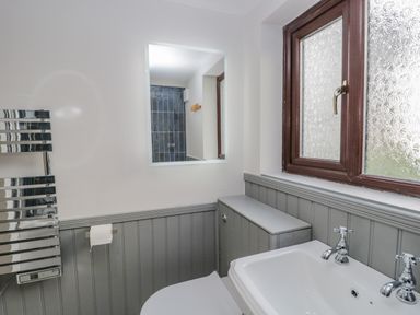 A bathroom with a sink toilet paper holder window and wall mirror at Ashness in Bassenthwaite near Keswick