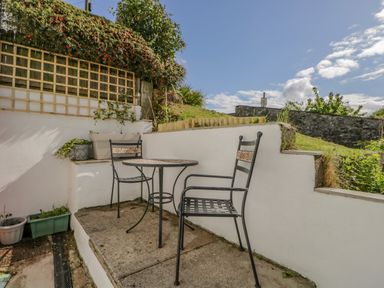 An outdoor patio area with two metal chairs and a round table surrounded by white walls and greenery at Ashness Bassenthwaite near Keswick