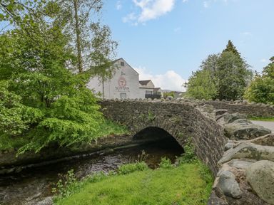 A stone arch bridge over a small river with trees and a building with sun inn signage at Ashness in Bassenthwaite near Keswick