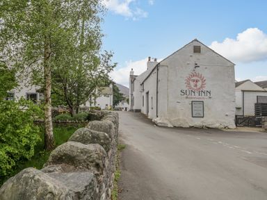 A street view with a white building featuring sun inn signage and a stone wall with trees at Ashness Bassenthwaite near Keswick