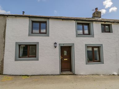 The front exterior of a white house with four windows and a wooden door with a sign above it saying Ashness at Ashness in Bassenthwaite near Keswick