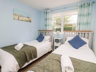 A bedroom with two single beds green throws and blue pillows at Cwtsh Cragen in New Quay