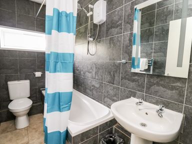 A bathroom with a toilet sink bathtub shower and a blue and white striped shower curtain at Cwtsh Cragen in New Quay