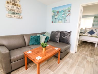 A living room with a gray sofa and wooden coffee table next to a bedroom at Cwtsh Cragen in New Quay