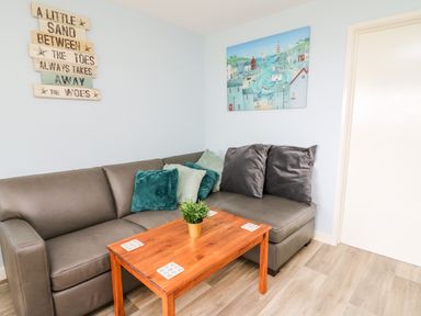A corner of a living room with a gray sectional sofa with cushions and a wooden coffee table with a small plant at Cwtsh Cragen in New Quay