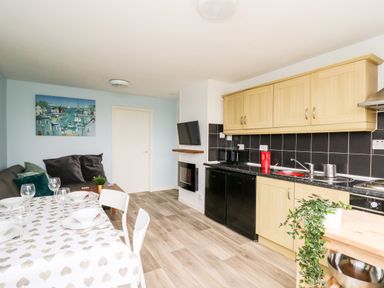 A kitchen and dining area with wooden cabinets a table set with plates and glasses a sofa with cushions and a wall painting at Cwtsh Cragen in New Quay