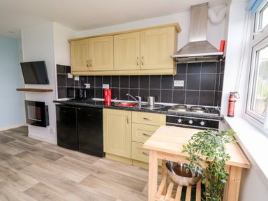 A kitchen with wooden cabinets black backsplash and appliances including microwave stove and refrigerator at Cwtsh Cragen in New Quay