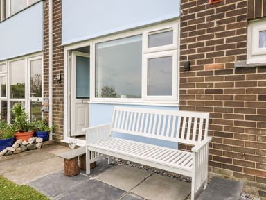 An outdoor bench and small table with a glass on a paved patio outside a house at Cwtsh Cragen in New Quay