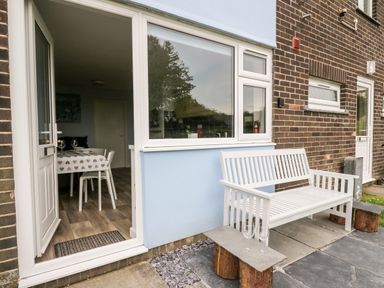 An outdoor patio area with a white bench and a small table holding two wine glasses next to a door opening to a dining area at Cwtsh Cragen in New Quay