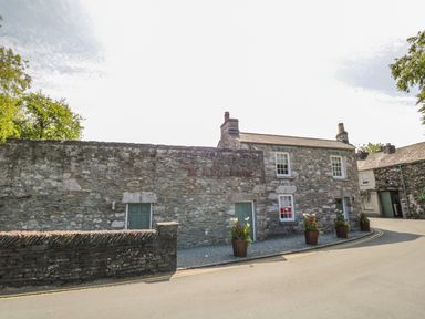 A stone building with green doors and flower pots outside on a street at 1 Tower House in Cartmel