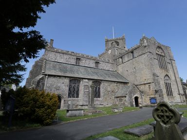 A stone church with a clock tower surrounded by gravestones and a paved pathway at 1 Tower House in Cartmel