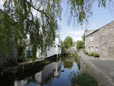 A small river with stone and white houses on either side and a stone bridge in the background at 1 Tower House in Cartmel