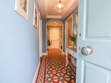 A hallway with blue walls a patterned tile floor a white door at the end and a table with flowers at 1 Tower House in Cartmel