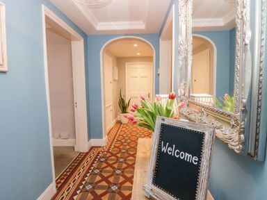 A hallway with blue walls patterned floor a bouquet of tulips and a welcome sign at 1 Tower House in Cartmel