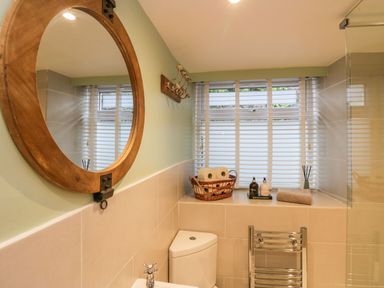 A bathroom with a round wooden mirror a toilet a basket with toilet paper and bottles on the windowsill and a towel rack at 1 Tower House in Cartmel