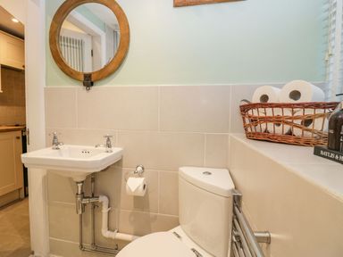 A bathroom with a corner toilet and wall mounted sink with a round mirror above at 1 Tower House in Cartmel