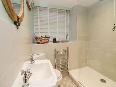 A bathroom with a sink a toilet a shower area and a window with blinds at 1 Tower House in Cartmel