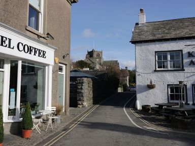 A street with a coffee shop patio and white buildings and a church in the background at 1 Tower House in Cartmel