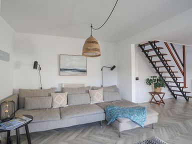A living room with a gray sectional sofa and a blue throw next to wooden stairs at Disgwylfa in Moelfre