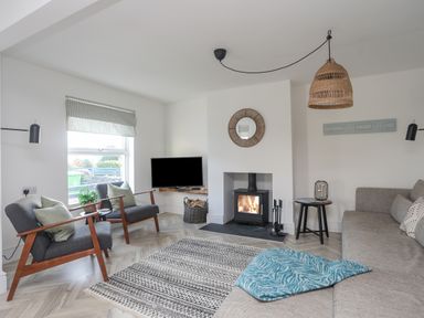 A living room with two armchairs a sofa a fireplace and a television at Disgwylfa in Moelfre