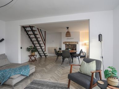 A living area with a sofa a chair a round dining table with chairs and a staircase at Disgwylfa in Moelfre