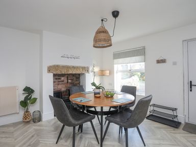 A dining area with a round wooden table and four gray chairs near a brick fireplace at Disgwylfa in Moelfre
