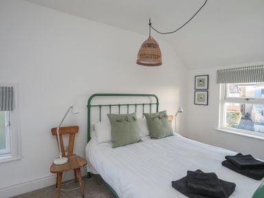 A bedroom with a green metal bed frame white bedding wooden chairs as bedside tables with lamps and framed bird pictures on the wall at Disgwylfa in Moelfre