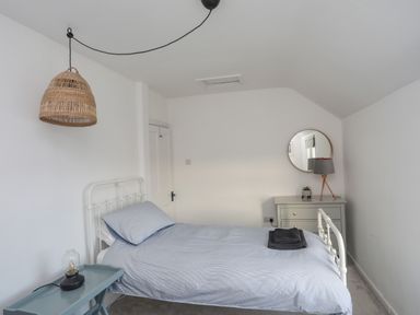 A bedroom with a single bed a blue bedside table a rattan hanging lamp and a dresser with a round mirror at Disgwylfa in Moelfre
