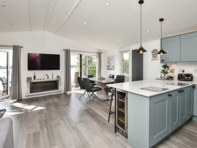 An open plan kitchen and dining area with blue cabinets a dining table with black chairs and a wall mounted television at Gerrida Lodge in South Lakeland Leisure Village near Tewitfield
