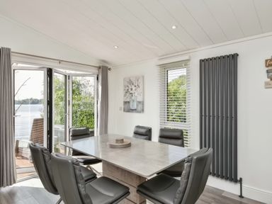 A dining room with six black chairs around a rectangular table near folding glass doors and windows at Gerrida Lodge South Lakeland Leisure Village near Tewitfield