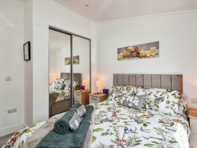 A bedroom with a bed with floral bedding a mirrored wardrobe and bedside tables with lamps at Gerrida Lodge South Lakeland Leisure Village near Tewitfield