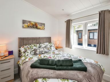 A bedroom with a bed floral bedding bedside tables with lamps and a window with curtains at Gerrida Lodge in South Lakeland Leisure Village near Tewitfield
