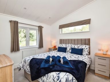 A bedroom with a bed with patterned bedding two bedside tables with lamps and a window with curtains at Gerrida Lodge South Lakeland Leisure Village near Tewitfield