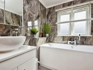A bathroom with a bathtub a sink with a cabinet and a window with blinds at Gerrida Lodge in South Lakeland Leisure Village near Tewitfield