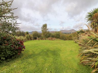 A green lawn with bushes and trees around and mountains in the background at Seascape Lodge in Kenmare County Kerry