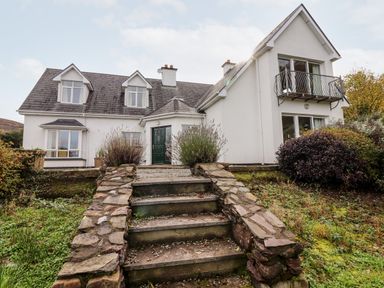 A white two-story house with stone steps leading to a green door surrounded by plants at Seascape Lodge in Kenmare County Kerry