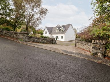 A white house with a grey roof behind stone walls and a paved driveway at Seascape Lodge in Kenmare County Kerry