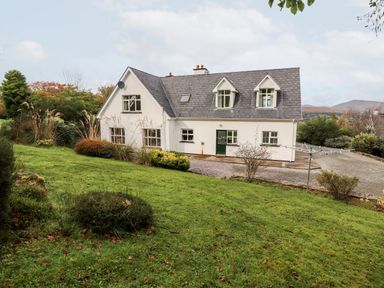 A two story house with a gray roof and white walls surrounded by grass and bushes at Seascape Lodge in Kenmare County Kerry