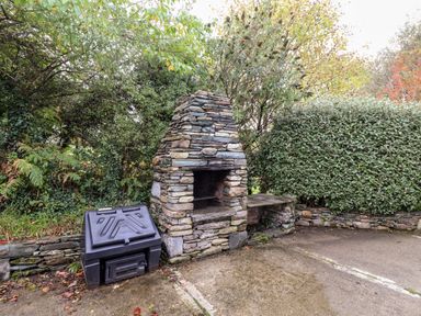 An outdoor stone barbecue grill next to a black storage box surrounded by green bushes at Seascape Lodge Kenmare County Kerry