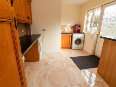 A utility room with wooden cabinets washing machines a sink a fire extinguisher a door and windows at Seascape Lodge in Kenmare County Kerry