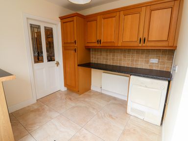 A kitchen with wooden cabinets tiled floor and a white door at Seascape Lodge in Kenmare County Kerry