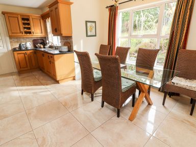 A kitchen with wooden cabinets and a dining area with a glass table and wicker chairs at Seascape Lodge Kenmare County Kerry