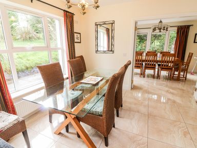 A dining area with a glass table and wicker chairs next to a window and another wooden dining table with chairs in the adjoining room at Seascape Lodge Kenmare County Kerry