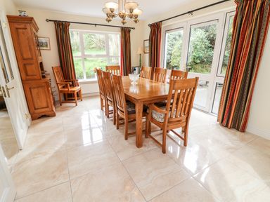 A dining room with a wooden table and chairs near windows and glass doors at Seascape Lodge in Kenmare County Kerry