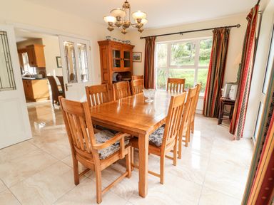 A dining room with a wooden dining table and chairs a cabinet and a large window with curtains at Seascape Lodge in Kenmare County Kerry